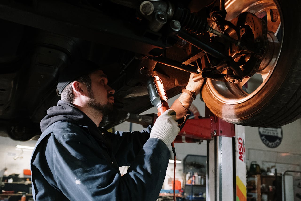 why-choose-us-01 Mechanic examining cars undercarriage at a garage, focusing on vehicle maintenance.
